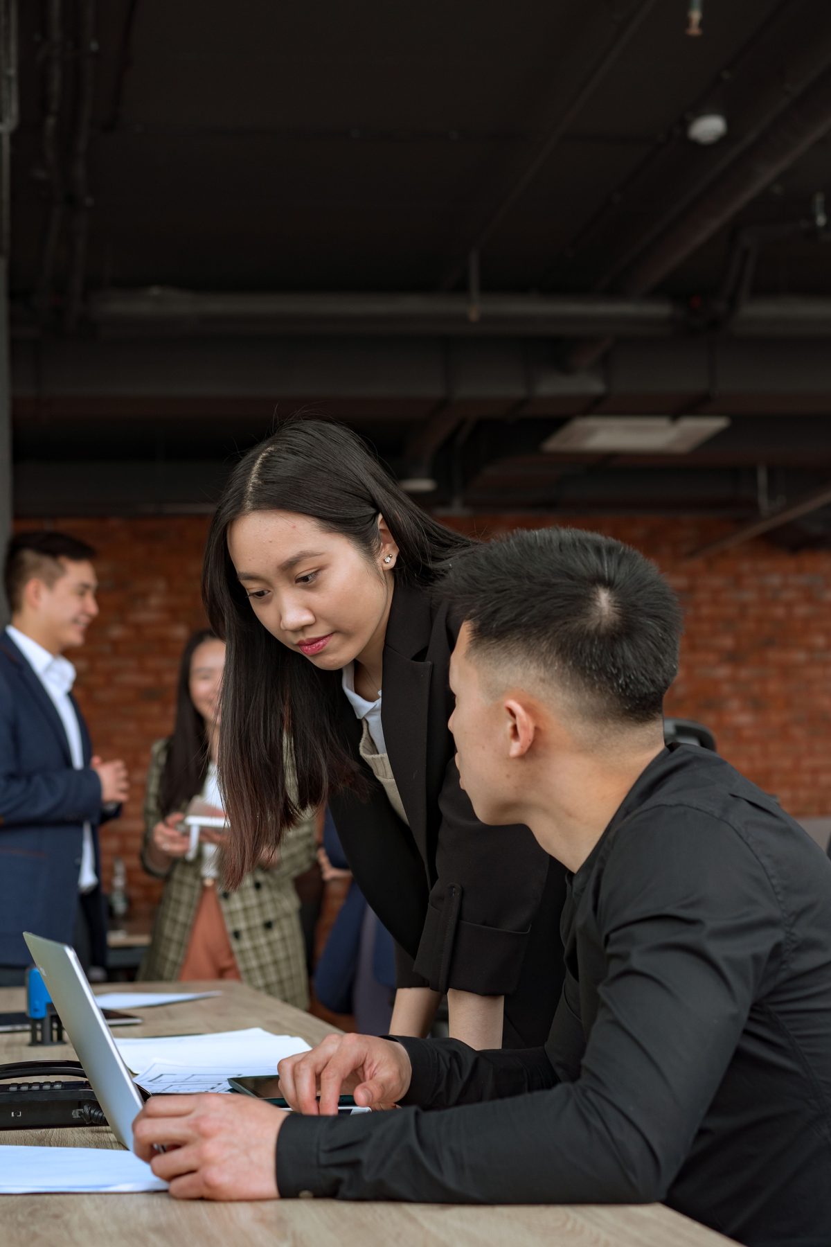 A colleague leans in to go through a teammate’s work with him at his laptop